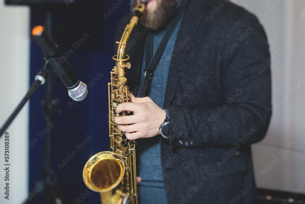 Fototapeta premium Concert view of saxophonist, a saxophone sax player with vocalist and musical band during jazz orchestra show performing music on a stage in the scene lights
