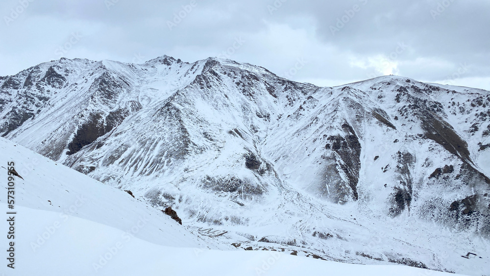 Aerial view of snow-covered mountain slopes, ridges and peaks. Hiking in the mountains in winter. Grey sky.