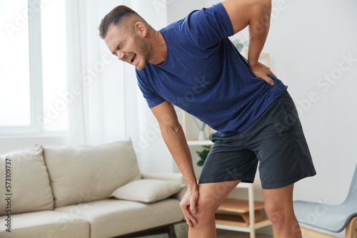 Man backache neck and shoulder pain, inflammation of muscles and ligaments rupture during sports, inflammation and injury, in a blue t-shirt at home