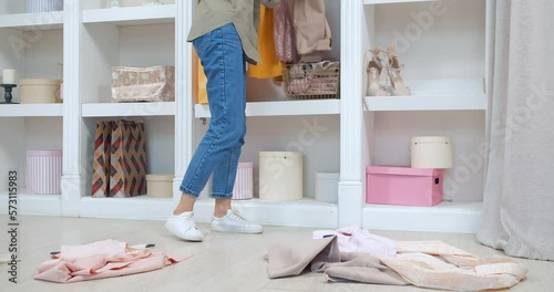 Young woman picking up clothes scattered on the floor and putting them in a closet in a dressing room or store