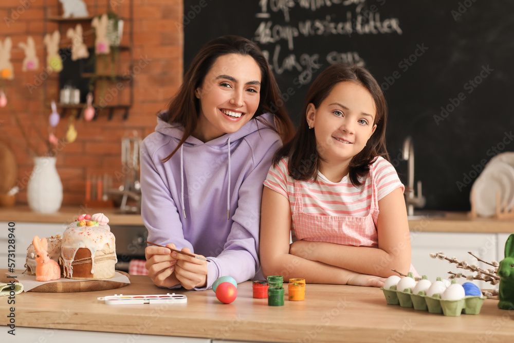 Fototapeta premium Little girl and her mother painting Easter eggs at table in kitchen