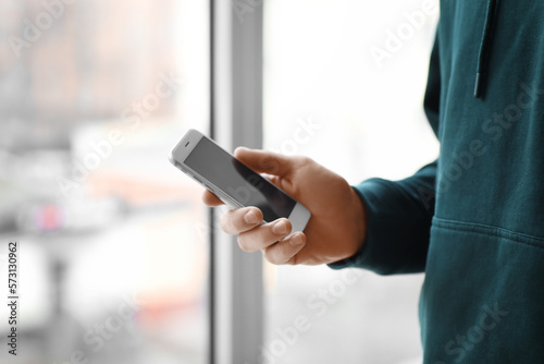 Young man with modern mobile phone near window, closeup