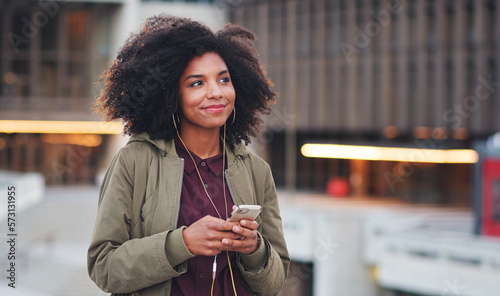 Music, travel and phone with black woman in city for streaming, happy and social media. Technology, afro and smile with girl walking and listening to earphones for mobile radio, network or podcast photo