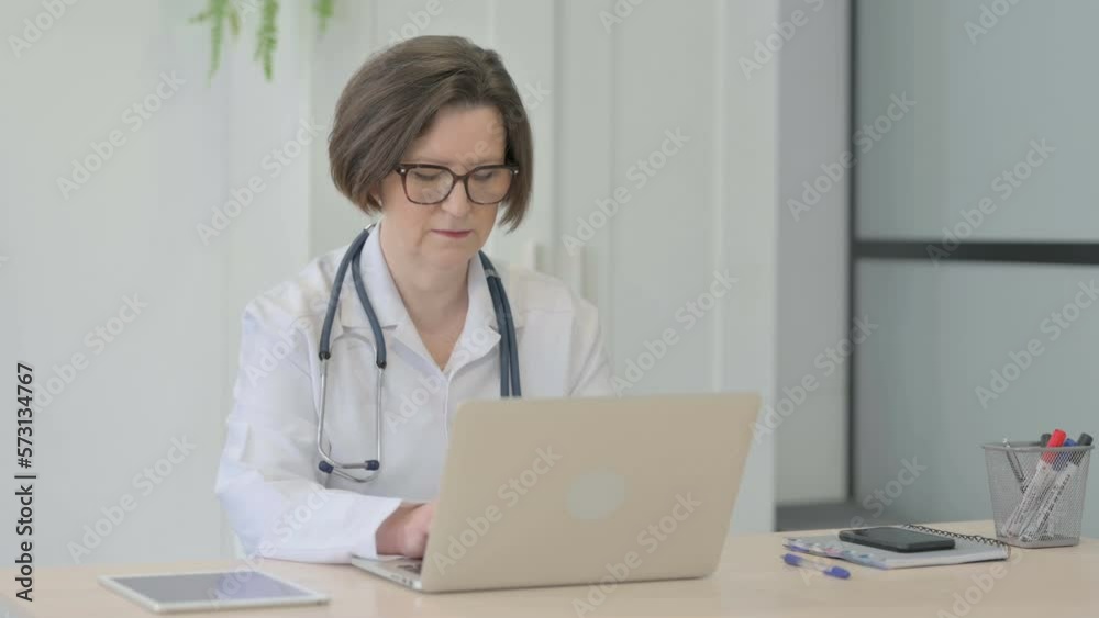 Old Female Doctor Typing on Laptop in Clinic Old Female Doctor Typing on Laptop in Clinic