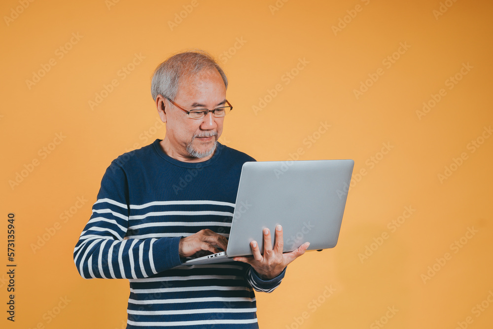 Asian senior man using laptop computer for working after retirement on the yellow background.