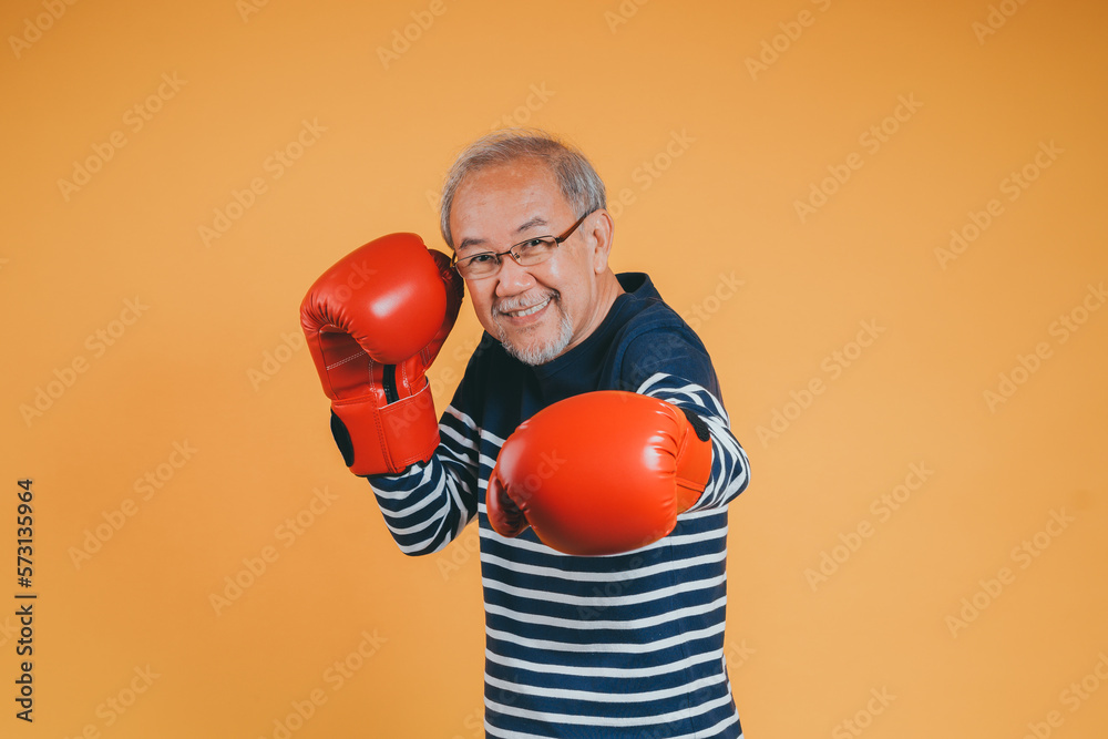 Asian senior man with boxing glove on the yellow background. Asian senior man with boxing glove on the yellow background.