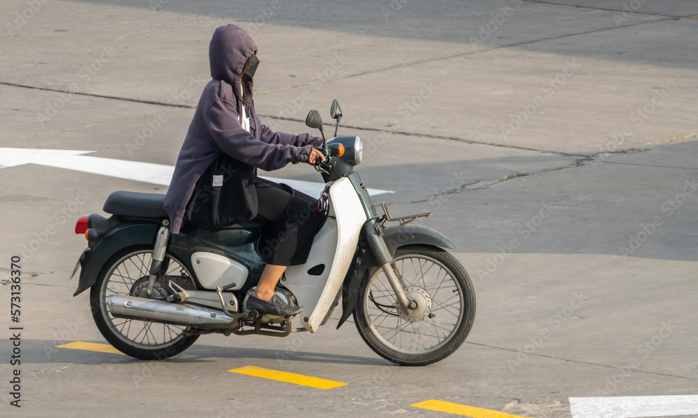 A woman with a hood rides a motorcycle