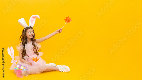 Festive Easter. A happy little girl is sitting and enjoying the spring holiday. A child with rabbit ears on a yellow isolated background. Copy space.
