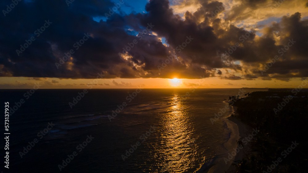Obraz premium aerial drone image of beautiful beach during sunset in Punta Cana. the golden sunset feels the sky with crimson orange and crystal clear water 