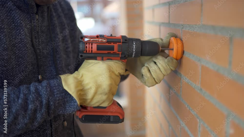 Man with an electric drill making a hole in the brick wall.