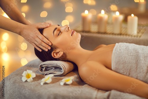 Close up portrait of a beautiful young woman lying with closed eyes and having face or head massage in spa. Woman relax enjoying health therapy treatment. Wellness and beauty day concept.