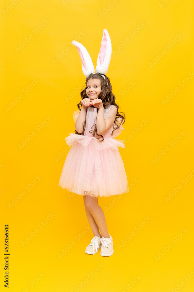 Festive Easter. A teenage girl in a fluffy dress and with rabbit ears is smiling broadly. A beautiful little girl in a rabbit costume on a yellow isolated background, full-length. Festive Easter. A teenage girl in a fluffy dress and with rabbit ears is smiling broadly. A beautiful little girl in a rabbit costume on a yellow isolated background, full-length.