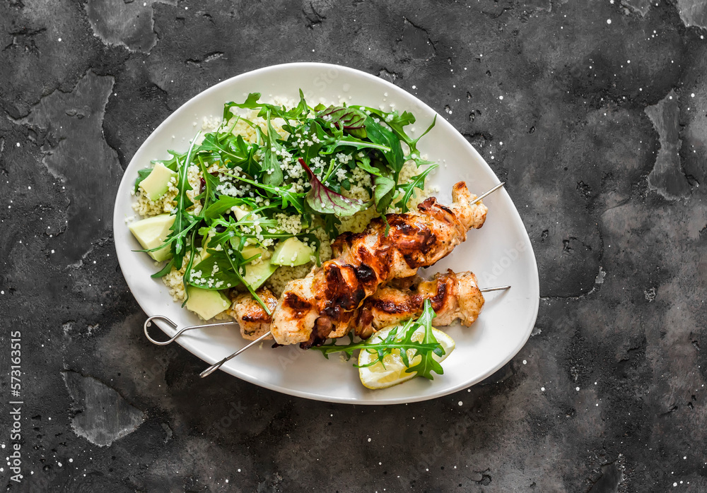 Delicious lunch, dinner - chicken bacon skewers and couscous, avocado, arugula salad on a dark background top view Delicious lunch, dinner - chicken bacon skewers and couscous, avocado, arugula salad on a dark background top view