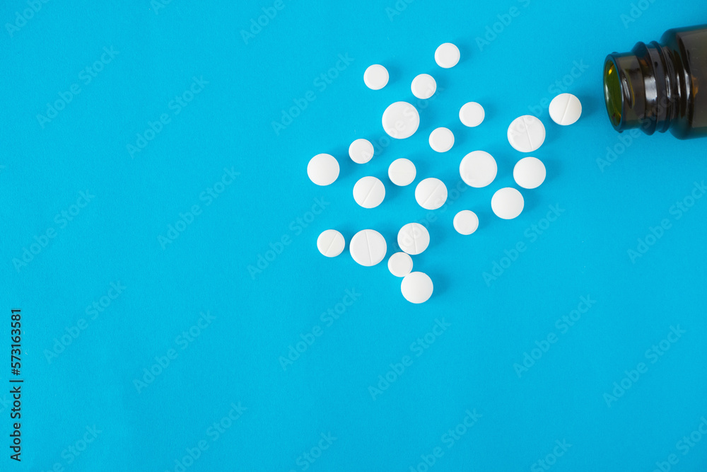 Scattered medicine white pills and glass container at blue background with copy space Scattered medicine white pills and glass container at blue background with copy space