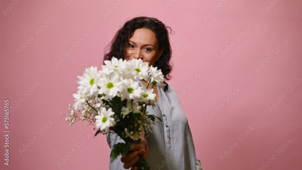 Attractive positive African American woman showing silence sign, winking and presenting to you a cute bouquet of white flowers, smiling and moving to music over pink color background Attractive positive African American woman showing silence sign, winking and presenting to you a cute bouquet of white flowers, smiling and moving to music over pink color background