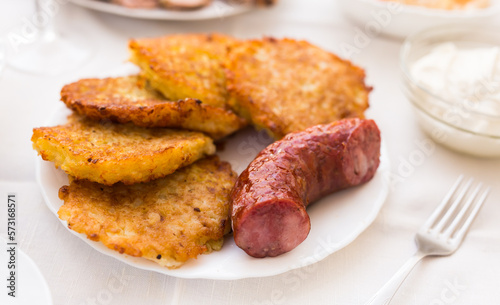 Potato pancakes with fried sausage on white plate