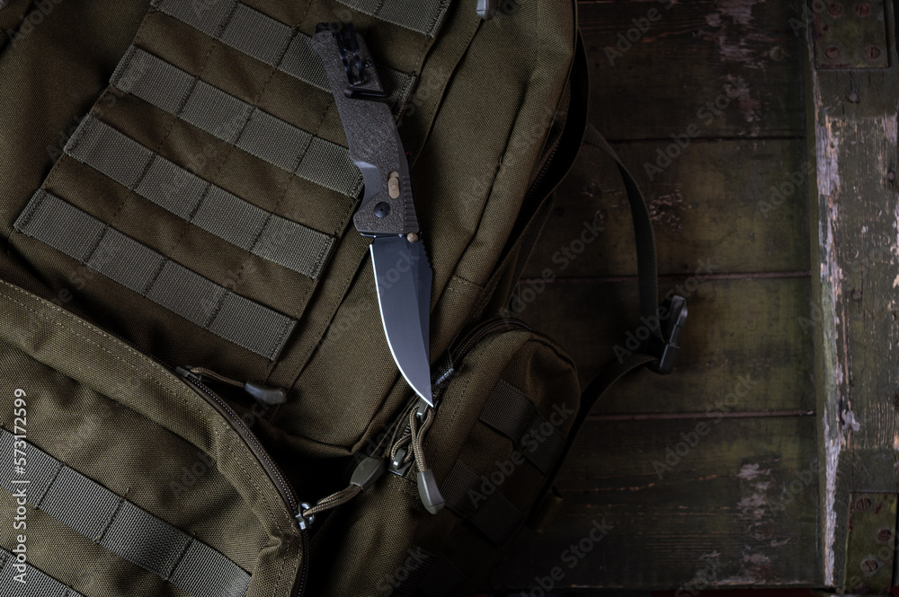 Folding sharp army knife on a military backpack. Knife with clip and