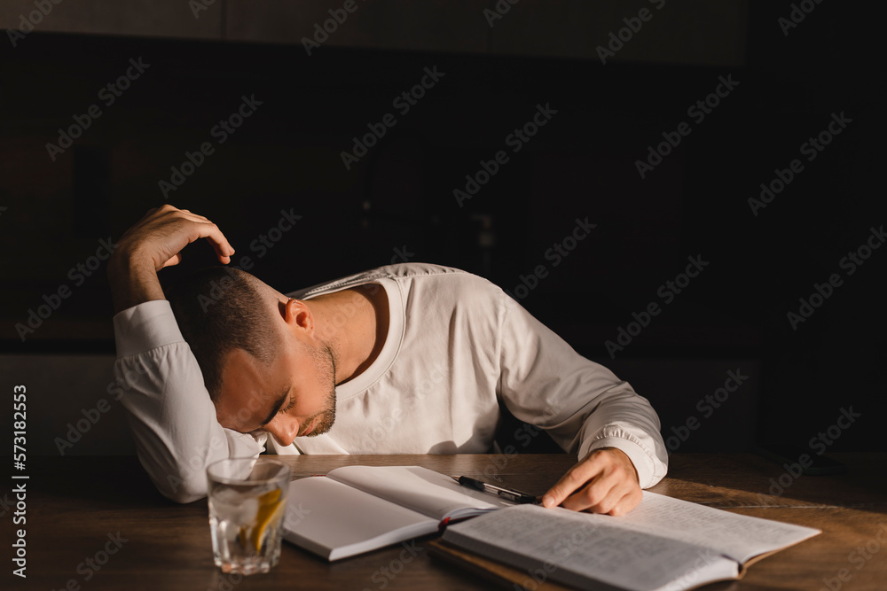 Obraz premium Bored man in white long sleeves tired when studying at home, he sitting on the table with paper notebook and sleeping. Male feeling sleepy and bored.