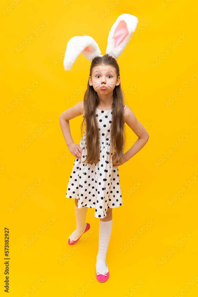 Cute girl in fancy Easter bunny ears and painted mustache on a yellow isolated background, Easter spring holiday. A girl in the ears of an Easter bunny.