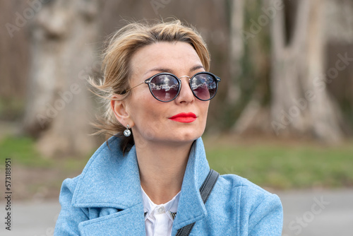 portrait of a stylish blonde 40-45 years old with glasses on a blurry background of nature. © Anelo