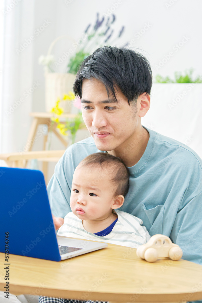 家で赤ちゃんとパソコンを見る父親 家で赤ちゃんとパソコンを見る父親