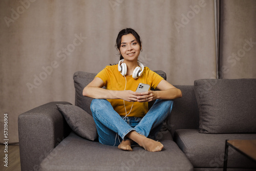 Happy indian or arabian girl resting on cozy sofa at home, listening to music