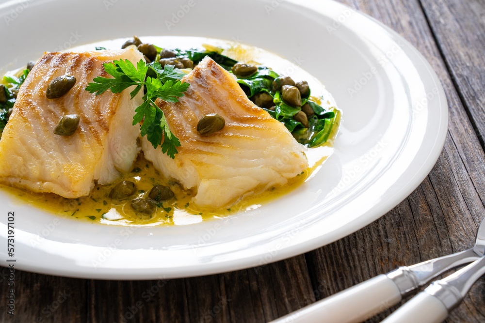 Fish dish - fried cod with spinach and capers in saffron sauce on wooden table
Fish dish - fried cod with spinach and capers in saffron sauce on wooden table