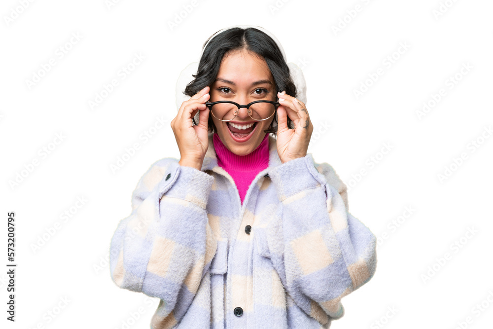 Young Argentinian woman wearing winter muffs over isolated background with glasses and surprised Young Argentinian woman wearing winter muffs over isolated background with glasses and surprised
