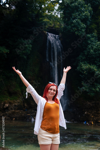 Beautiful happy smile girl with red hair enjoying life and beautiful nature. Behind the Abhesi Waterfall, Stones in the mountain river, Kutaisi, Georgia