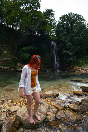 Beautiful girl with red hair enjoying life and beautiful nature. Behind the Abhesi Waterfall  Stones in the mountain river  Kutaisi  Georgia. Vertical photo.