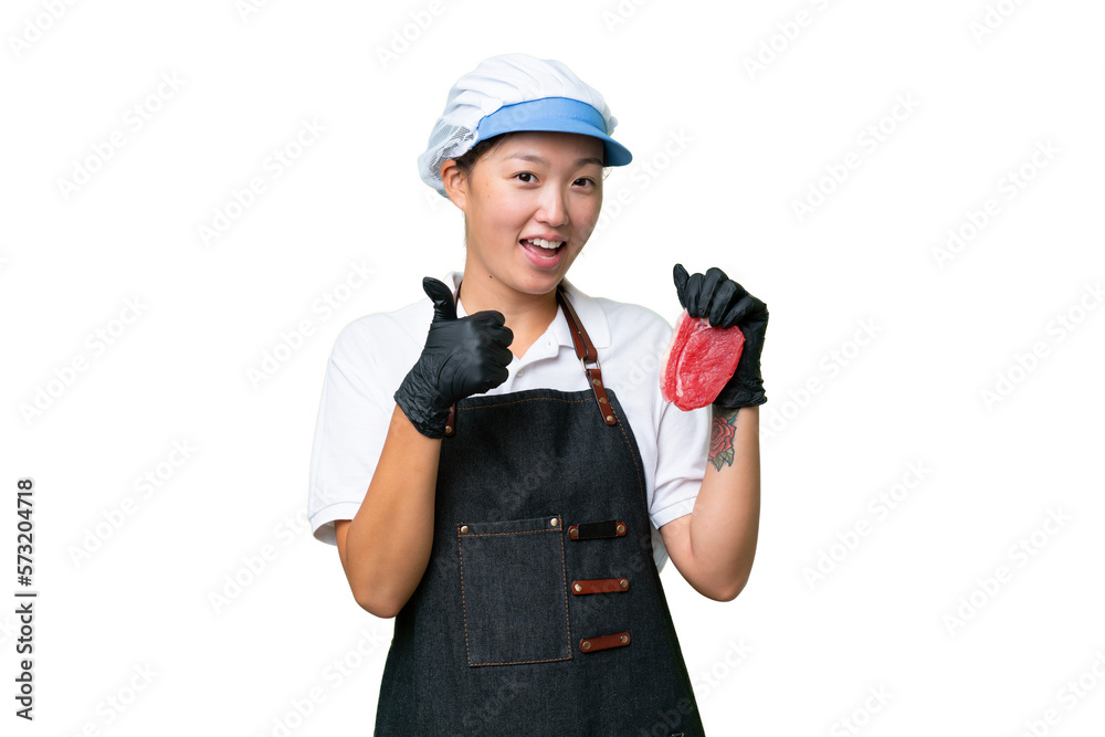 Young caucasian woman wearing an apron and serving fresh cut meat over isolated background with thumbs up because something good has happened Young caucasian woman wearing an apron and serving fresh cut meat over isolated background with thumbs up because something good has happened