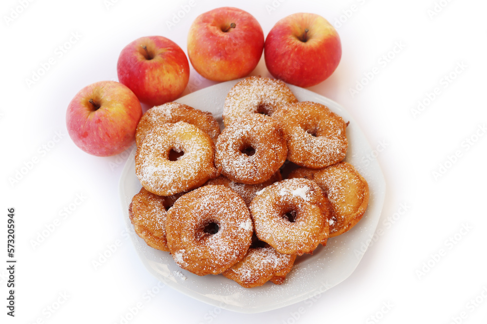 Homemade deep fried apple rings with batter sprinkled with powdered sugar on a plate isolated on white with fresh apples