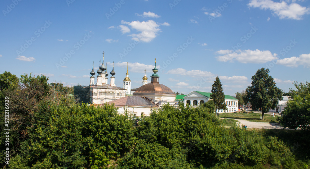 A beautiful urban landscape - a panoramic view of historical architecture with temples among green trees with lush foliage on a sunny summer day in Suzdal, Vladimir region and a space for copy