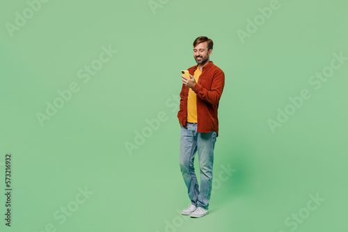 Full body side view smiling happy elderly man 40s year old he wears casual clothes red shirt t-shirt hold in hand use mobile cell phone isolated on plain pastel light green background studio portrait © ViDi Studio