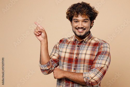 Fun Indian man wear brown shirt casual clothes point index finger aside indicate on workspace area copy space mock up isolated on plain pastel light beige background studio. People lifestyle concept.