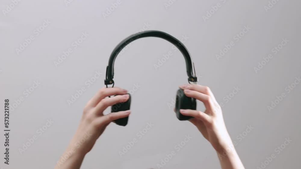 Hand close up holding black wireless headphones on gray background, opening and closing head phones. Hand close up holding black wireless headphones on gray background, opening and closing head phones.