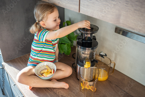 Little girl making fresh juice sitting on the table in home kitchen photo