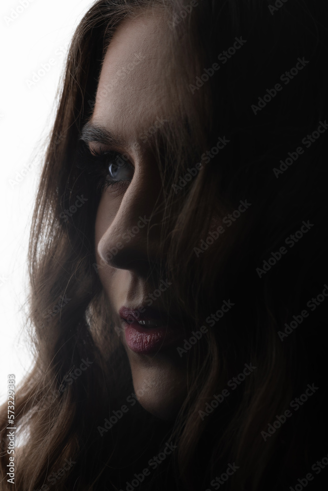 Fashion and make-up concept. Close-up dark face silhouette of beautiful and sexy woman with dark wavy hair. Part of model face illuminated with light. Sensual mood. Eye in camera focus Fashion and make-up concept. Close-up dark face silhouette of beautiful and sexy woman with dark wavy hair. Part of model face illuminated with light. Sensual mood. Eye in camera focus