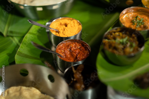 An assortment of traditional Indian seasonings — curry chilis; pickles; and 'gunpowder' splice blend ('milagai podi') — against a backdrop of banana leaves, suggesting southern Indian cuisine. photo