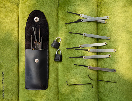 Many lock picking tools in a case, tension wrenches and 2 little padlocks flat lay. A kit of lock picks that can be used by a locksmith for opening doors or burglary