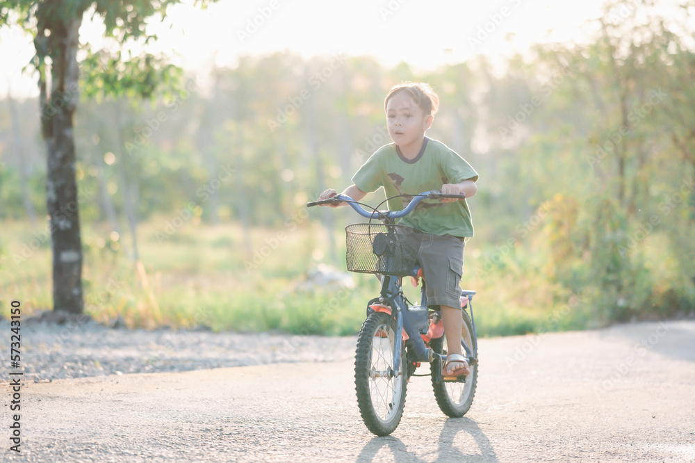 Cute little boy riding bicycle in the park at sunset time.