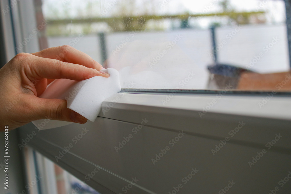 close up of a woman's hand cleaning a window with a white sponge 