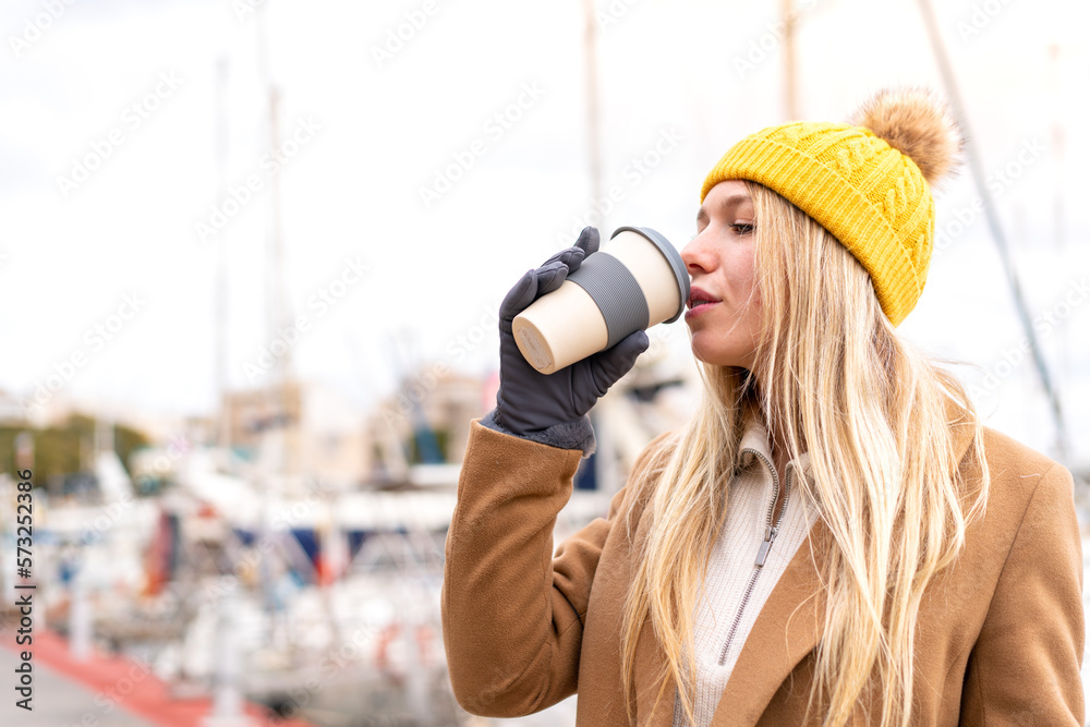 Young pretty blonde woman wearing winter jacket and holding a take away coffee at outdoors