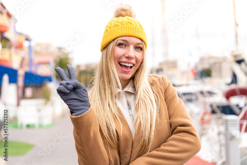 Young pretty blonde woman wearing winter jacket at outdoors smiling and showing victory sign
