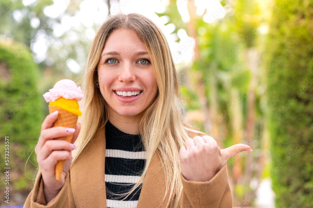 Young pretty blonde woman with a cornet ice cream at outdoors pointing to the side to present a product Young pretty blonde woman with a cornet ice cream at outdoors pointing to the side to present a product