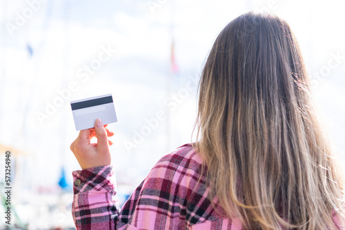 Young pretty Romanian woman holding a credit card at outdoors in back position