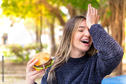 Young pretty Romanian woman holding a burger at outdoors has realized something and intending the solution