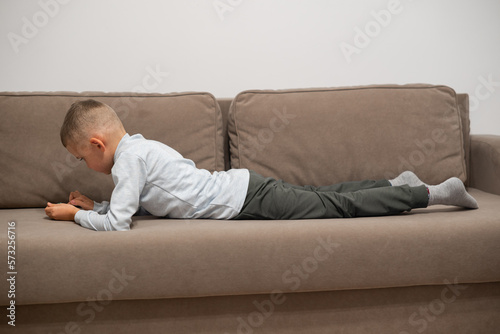Little boy playing mobile game on smartphone sitting on a sofa, top view. Child leisure at home, video gaming addiction © Oleg