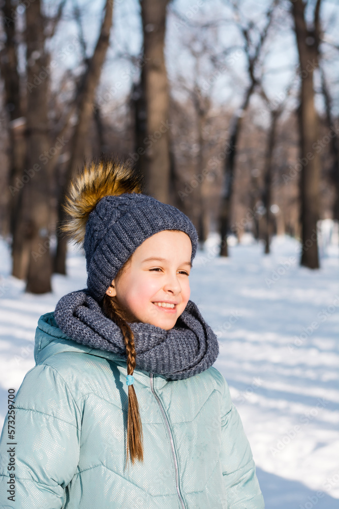 Portrait of a cheerful girl in warm clothes in a winter park on a frosty sunny day. Vertical view Portrait of a cheerful girl in warm clothes in a winter park on a frosty sunny day. Vertical view