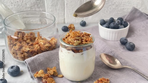 Yogurt with muesly granola and blueberries. Spoon with granola filling the jar.